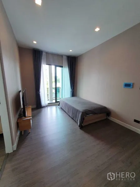 Detached House for rent in Khlong Luang, Pathum Thani - Cozy bedroom with single bed, balcony doors, TV stand and wood flooring.
