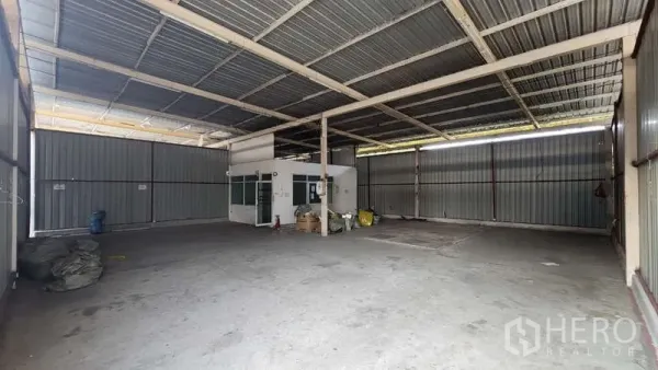 Warehouse for rent in Bang Khen, Bangkok - High-ceiling warehouse interior with steel frame, concrete floor, and a small office cabin.