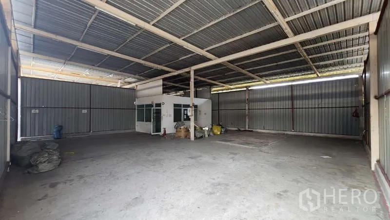 Warehouse for rent in Bang Khen, Bangkok - High-ceiling warehouse interior with steel frame, concrete floor, and a small office cabin.