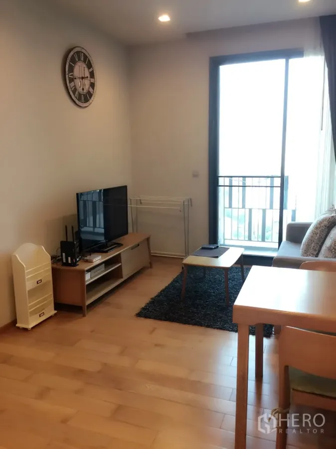 Condominium for rent in Khlong Toei, Bangkok - Bright living room with TV console, sofa, wood floors and a sliding glass door to the balcony in a Bangkok condo near BTS Thonglor.