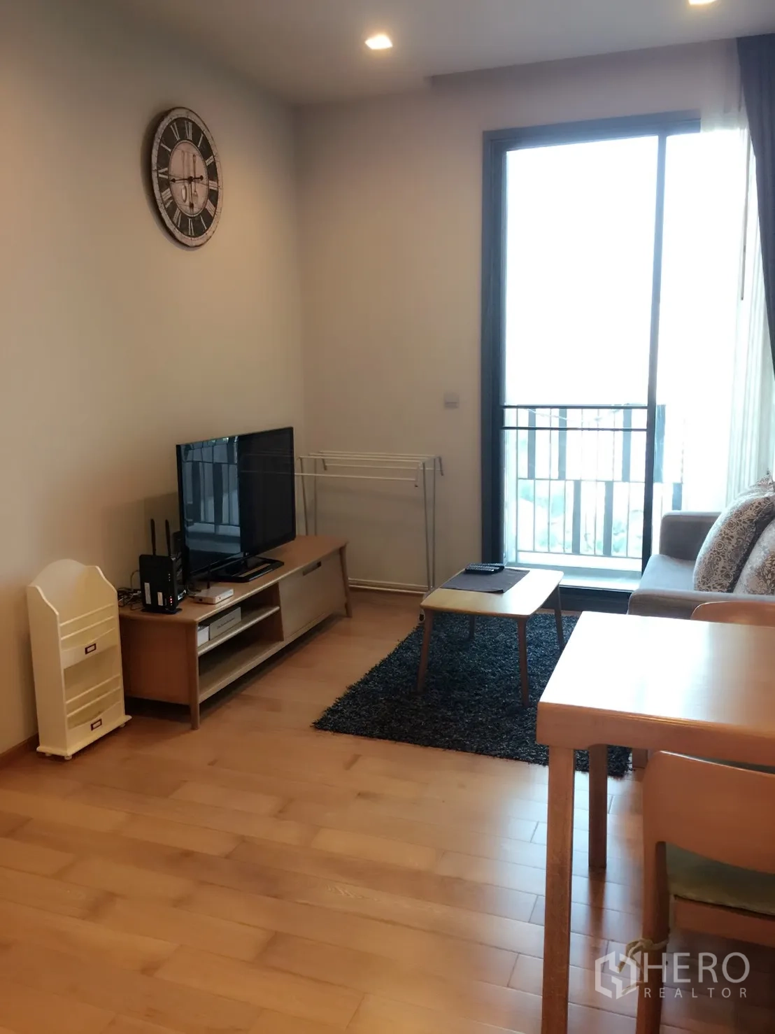 Condominium for rent in Khlong Toei, Bangkok - Bright living room with TV console, sofa, wood floors and a sliding glass door to the balcony in a Bangkok condo near BTS Thonglor.