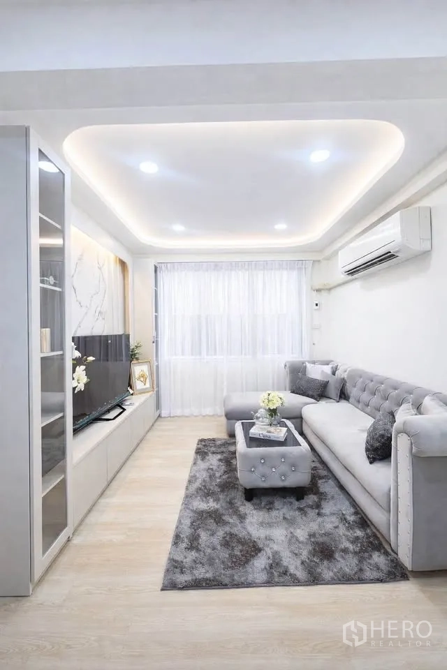 Detached House for rent in Huai Khwang, Bangkok - Living room with L-shaped sofa, TV cabinet, recessed ceiling lights and rug.