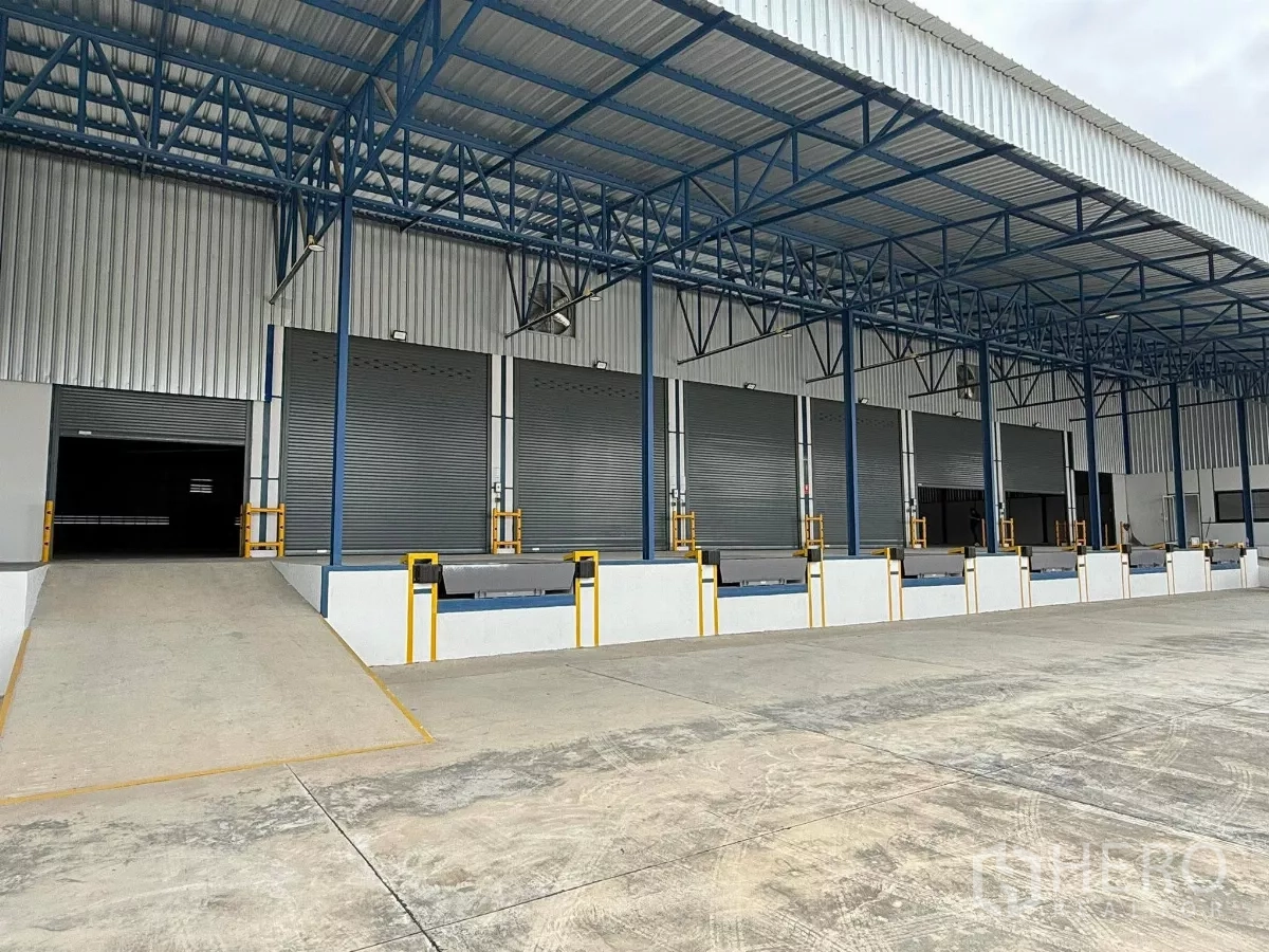 Warehouse for rent in Si Racha, Chon Buri - Row of six raised loading docks with dock levelers and a truck ramp at a modern facility.