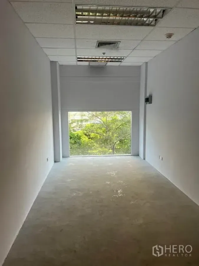 Retail Space for rent in Bang Rak, Bangkok - Narrow white retail unit with a large rear window overlooking trees, drop-ceiling lights and a concrete floor.