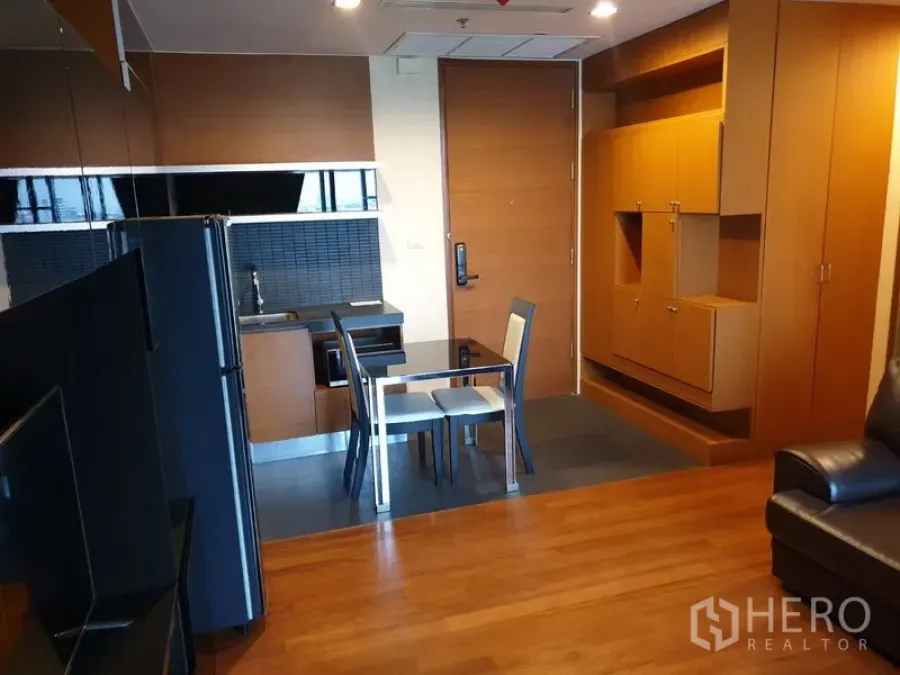 Condominium for rent in Khlong Toei, Bangkok - Open-plan kitchenette with black backsplash, glass dining table and built-in storage in a Bangkok condo.