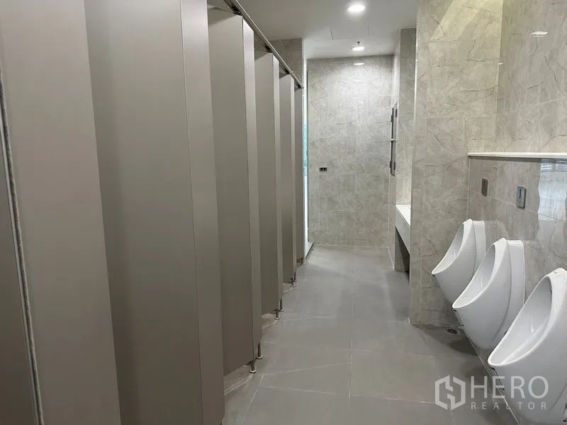 Office Space for rent in Ratchathewi, Bangkok - Restroom corridor with multiple stalls, urinals and stone-pattern tiles under bright lighting.