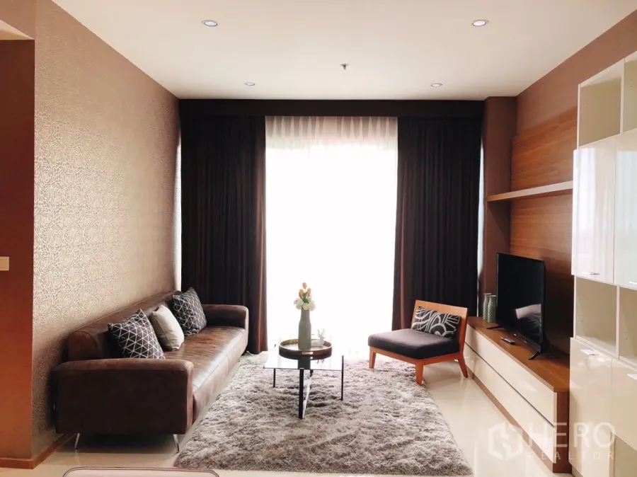 Condominium for rent in Khlong Toei, Bangkok - Bright living room with leather sofa, TV console, plush rug and floor‑to‑ceiling window.