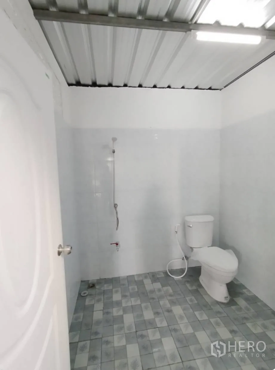 Warehouse for rent in Bang Khen, Bangkok - Clean warehouse restroom with white tiled walls, handheld shower, and ceramic toilet on a patterned tile floor.
