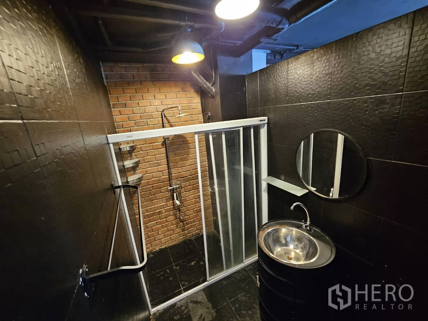 Office Space for rent in Watthana, Bangkok - Industrial-style bathroom with black tiles, glass shower enclosure, round steel sink and warm lighting.