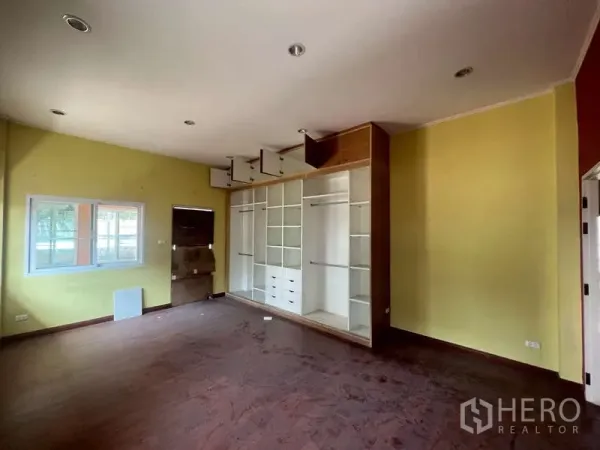 Detached House for rent in Watthana, Bangkok - Empty room with built-in white shelving and wood floors, yellow walls and a window.