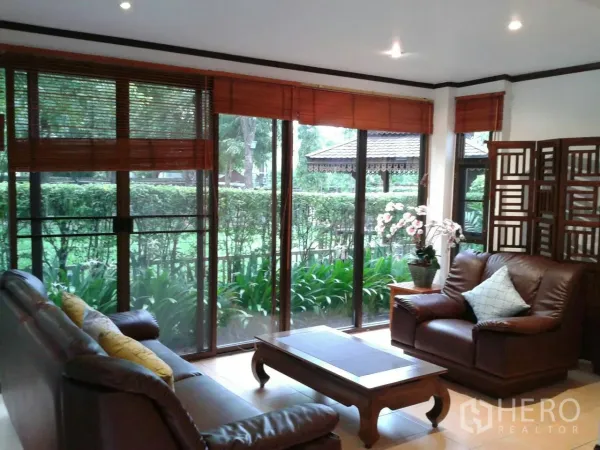 Detached House for rent in Suan Luang, Bangkok - Bright living room with leather sofas and floor-to-ceiling windows overlooking a landscaped garden.