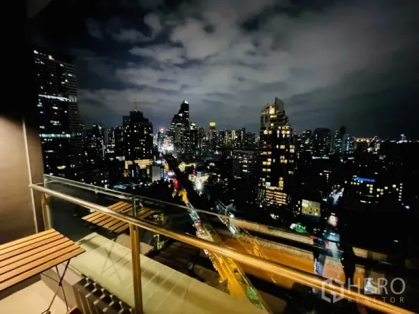 Condominium for rent in Khlong Toei, Bangkok - Private balcony at night overlooking Bangkok’s skyline with seating and glass railing.