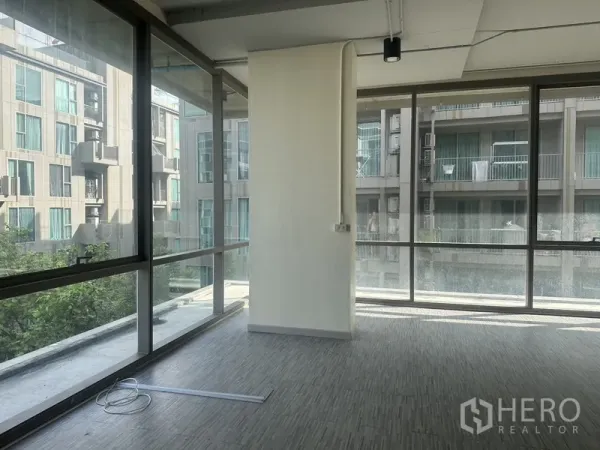 Office Space for rent in Phra Khanong, Bangkok - Corner workspace with wraparound glass, a central column, and views of neighboring residential buildings.