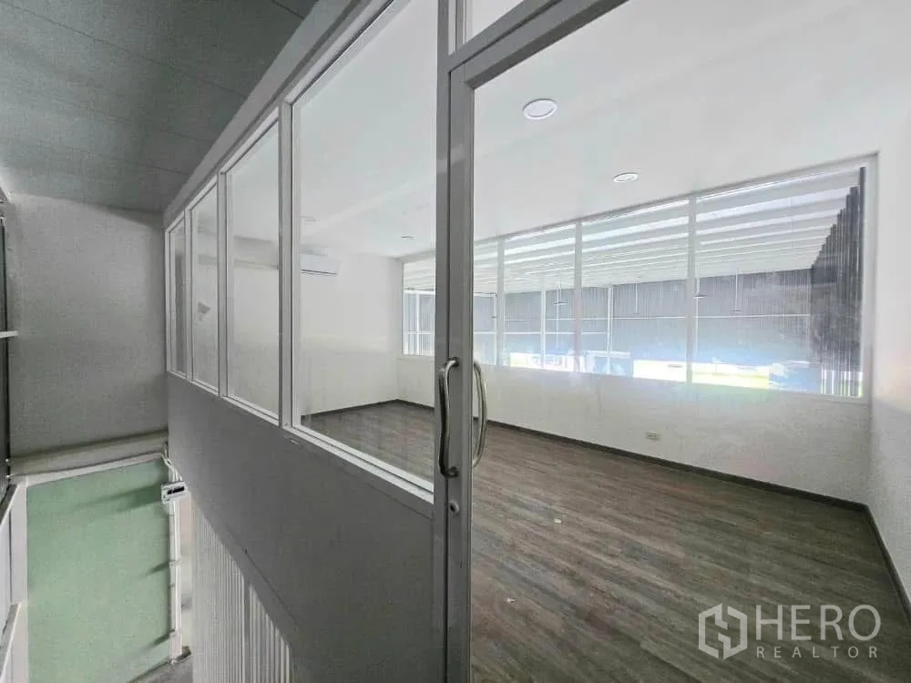 Warehouse for rent in Prawet, Bangkok - Glass-enclosed mezzanine office with sliding door, large windows and wood-look flooring.