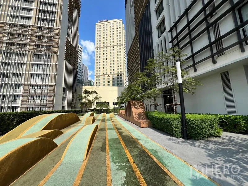 Condominium for sale - Landscaped outdoor terrace with sculpted mounds between high-rise buildings on a sunny day.