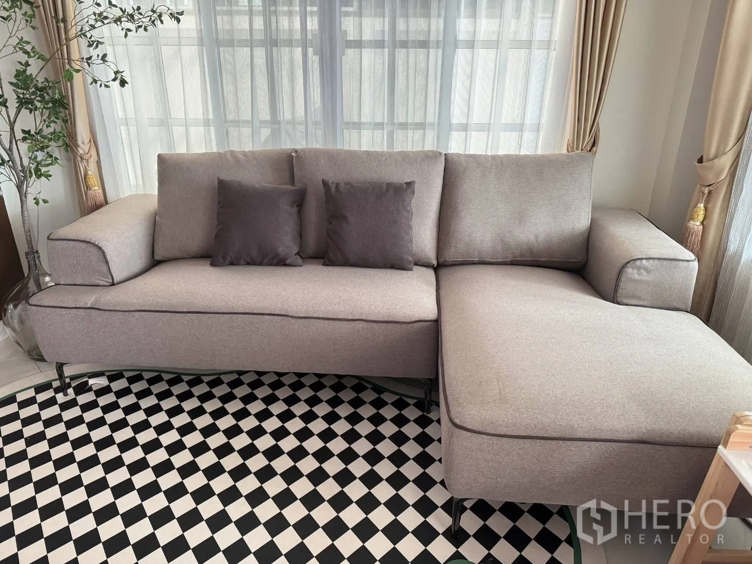 Detached House for rent in Mueang Samut Prakan, Samut Prakan - Bright living room with an L-shaped gray sofa, checkered rug and sheer curtains.