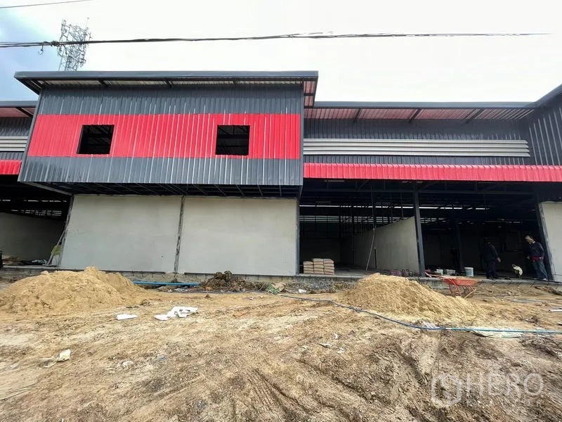 Warehouse for rent in Pathum Thani - Center facade of the warehouse with a large opening and earthworks in front.