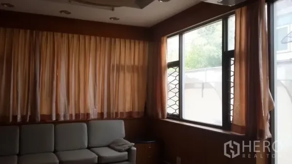 独立式住宅 出租或出售在Huai Khwang, Bangkok - 温馨客厅，L 型沙发、大幅窗帘与木质墙面。