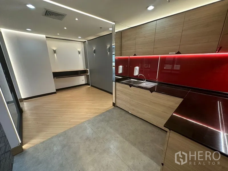 Office Space for rent in Khlong Toei, Bangkok - Modern office pantry with wood cabinets, red backsplash, and sink beside a lounge area.