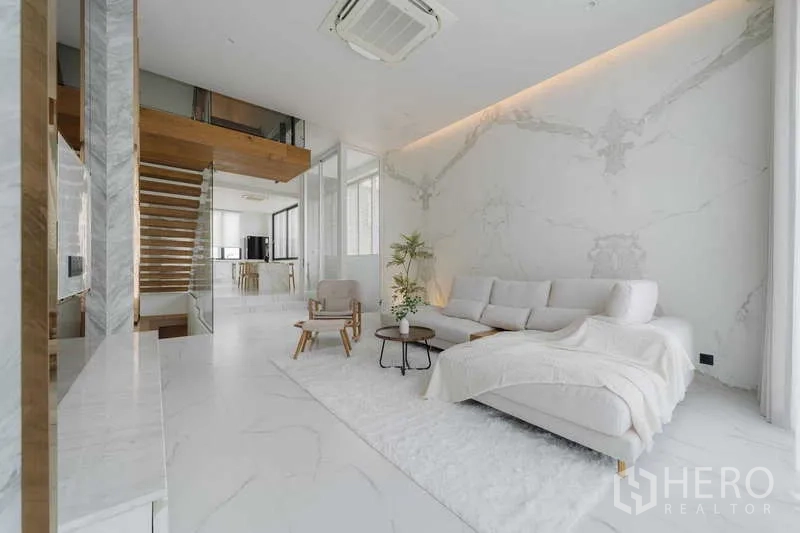 Townhouse for rent or sale in Watthana, Bangkok - Open-plan living room with marble floors, sectional sofa, and floating staircase to the kitchen.