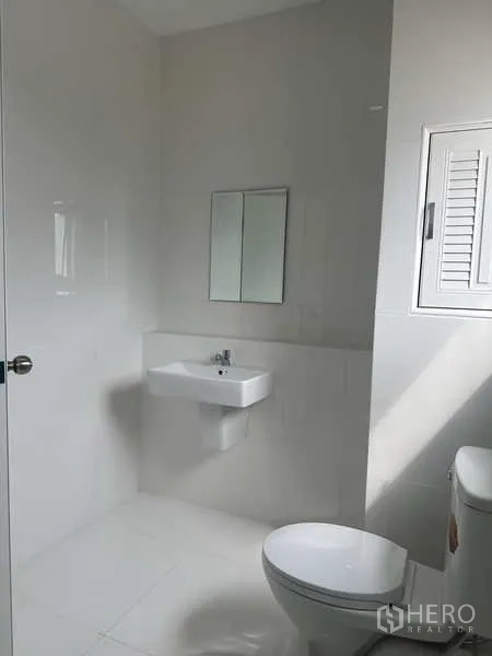 Factory for rent in Khlong Luang, Pathum Thani - Modern restroom with toilet, sink and a small window, finished in white tiles.