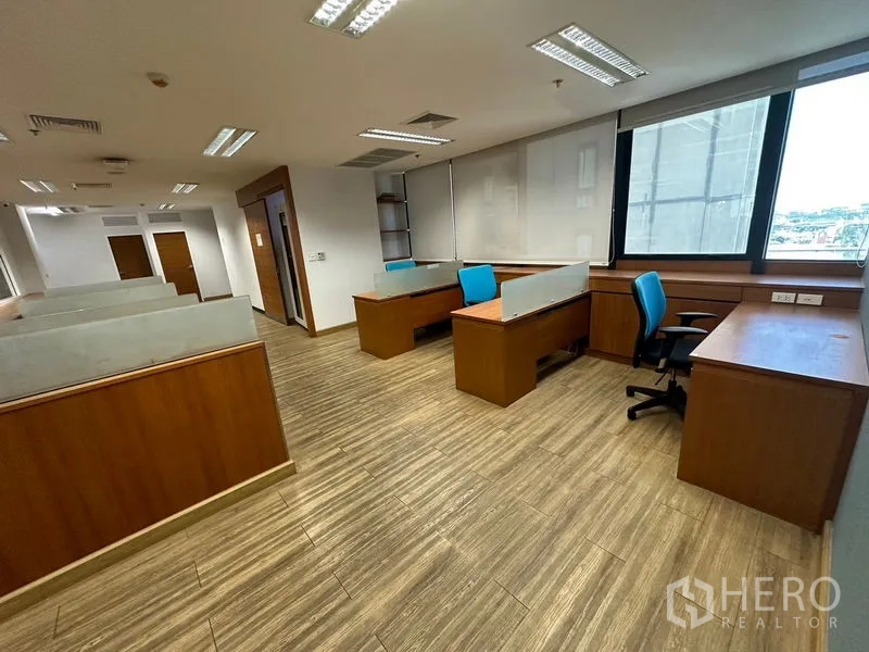 Office Space for rent or sale - Open-plan office with partitioned desks, large window and wood-look flooring.