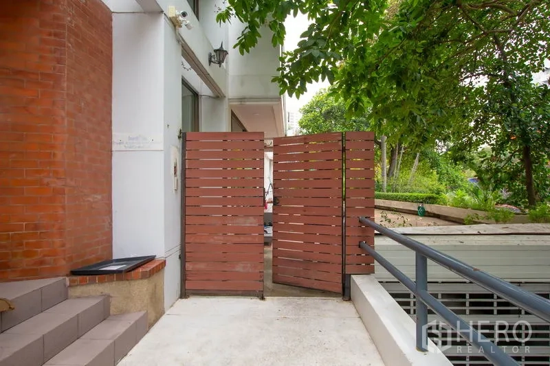 Townhouse for rent in Khlong Toei, Bangkok - Entrance area with wooden slat gate beside a brick wall and greenery.