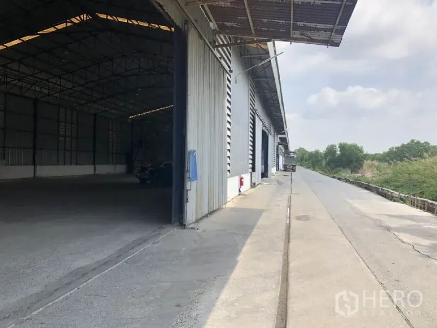 Warehouse for rent in Pathum Thani - Exterior loading bay of a large steel warehouse with a wide truck access road and canopy.