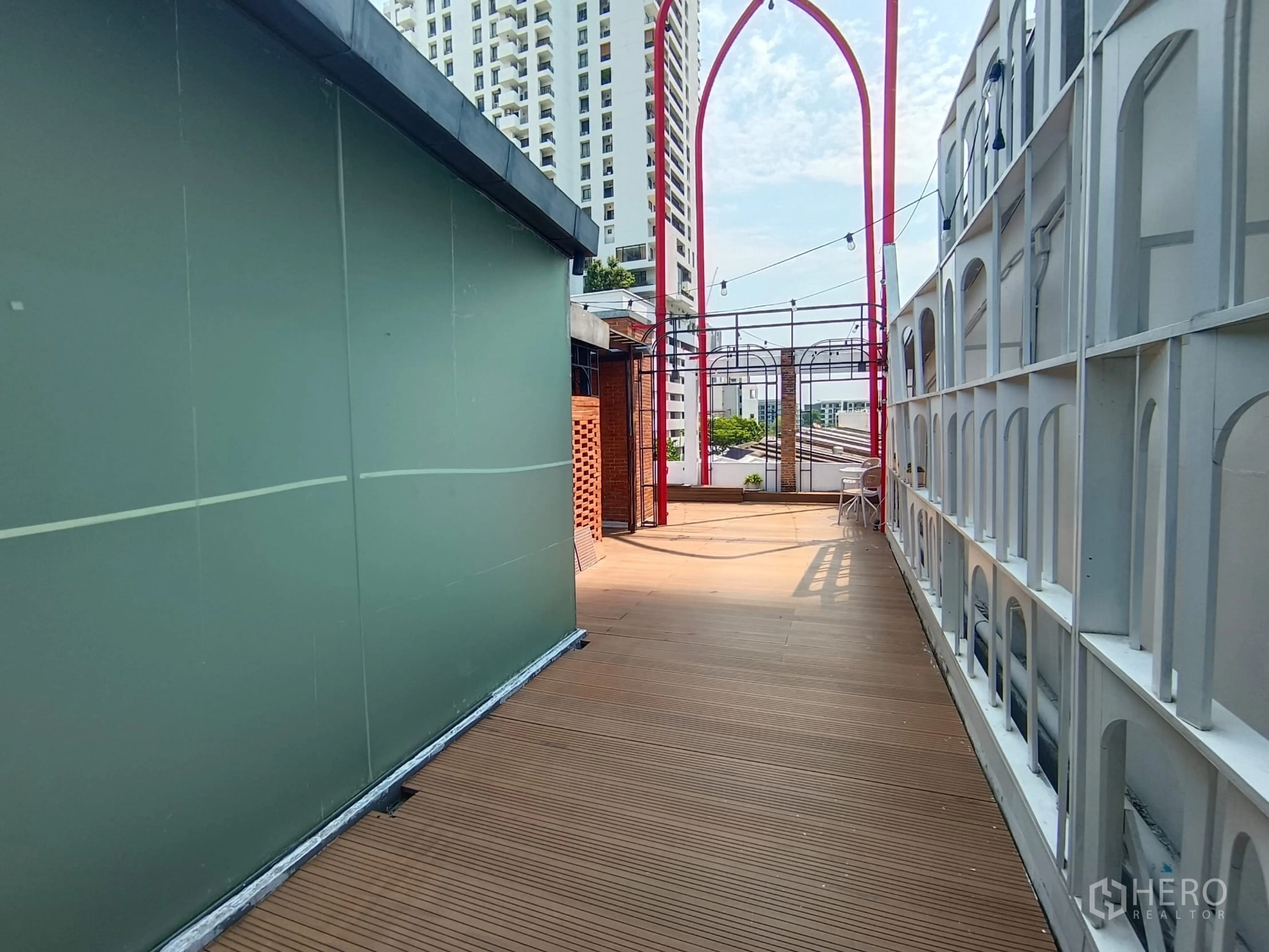 Shophouse for rent in Watthana, Bangkok - Rooftop terrace with wooden decking, string lights and city buildings in view.