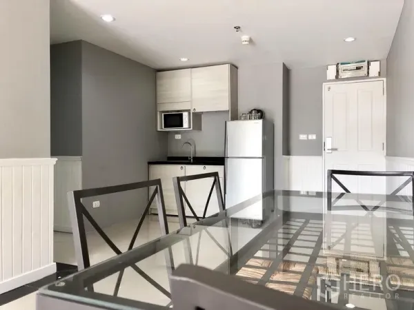 Condominium for rent in Khlong Toei, Bangkok - Compact kitchen with microwave, storage cabinets and full-size refrigerator beside a dining table.