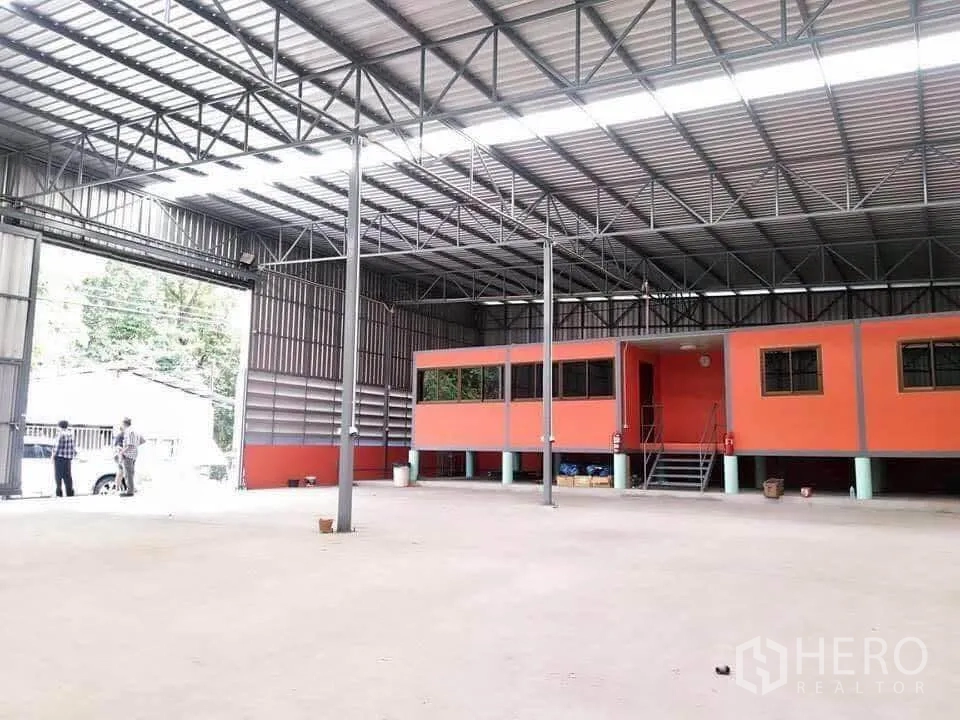 Warehouse for rent in Thanyaburi, Pathum Thani - Open-span warehouse interior with high steel truss roof, skylight panels, and an elevated orange mezzanine office.