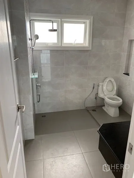 Townhouse for rent in Bang Na, Bangkok - Modern bathroom with rain shower, toilet and grey wall tiles beneath a window