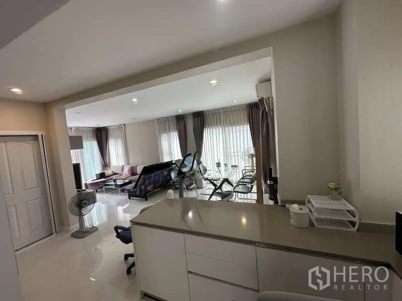 独立式住宅 出售在Sai Mai, Bangkok - 从厨房看向明亮客厅与落地窗窗帘。