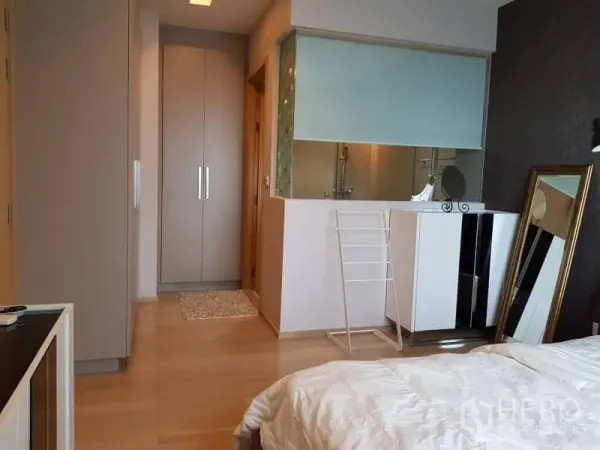 Condominium for rent in Khlong Toei, Bangkok - Bedroom with built-in wardrobes, vanity cabinet, and a glass partition to the bathroom.