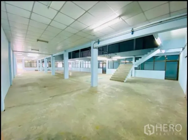 Factory for rent in Sam Phran, Nakhon Pathom - Large warehouse floor with support columns, stairs to a mezzanine and fluorescent lighting.