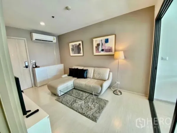 Condominium for rent in Khlong Toei, Bangkok - Modern lounge with sectional sofa, floor lamp, abstract wall art and a glass coffee table.