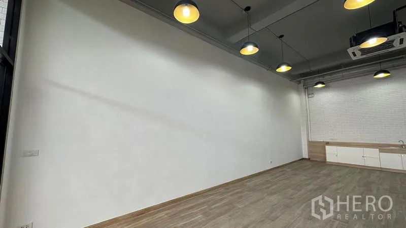 Retail Space for rent - Long white display wall, pendant lighting and spacious sales floor with wood-look tiles.