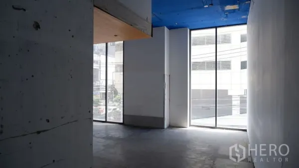 Retail Space for rent in Watthana, Bangkok - Empty retail interior with concrete floor, high blue ceiling, and floor-to-ceiling windows bringing natural light.