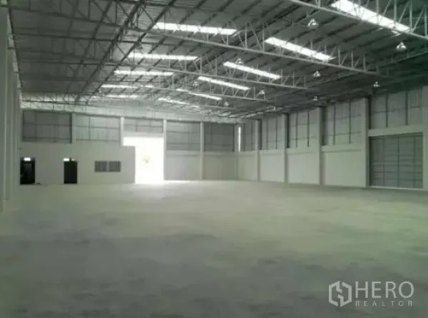 Warehouse for rent in Pathum Thani - Spacious warehouse interior with high steel truss roof, skylights, and smooth concrete floor.