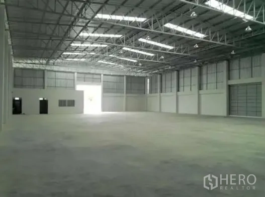 Warehouse for rent in Pathum Thani - Spacious warehouse interior with high steel truss roof, skylights, and smooth concrete floor.