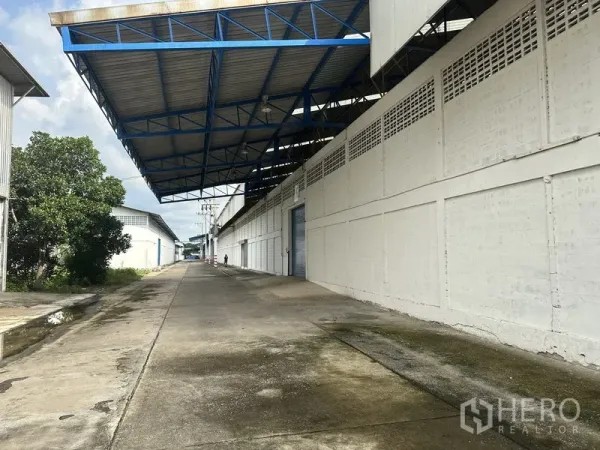 Factory for rent in Nonthaburi - Covered loading bay with blue steel canopy beside a long factory driveway.