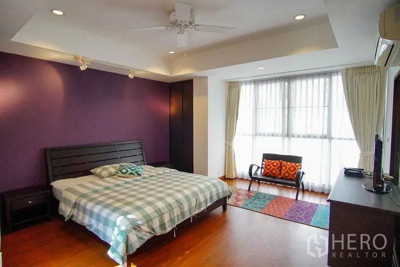 Townhouse for rent in Watthana, Bangkok - Spacious bedroom with purple accent wall, king bed, and large window.