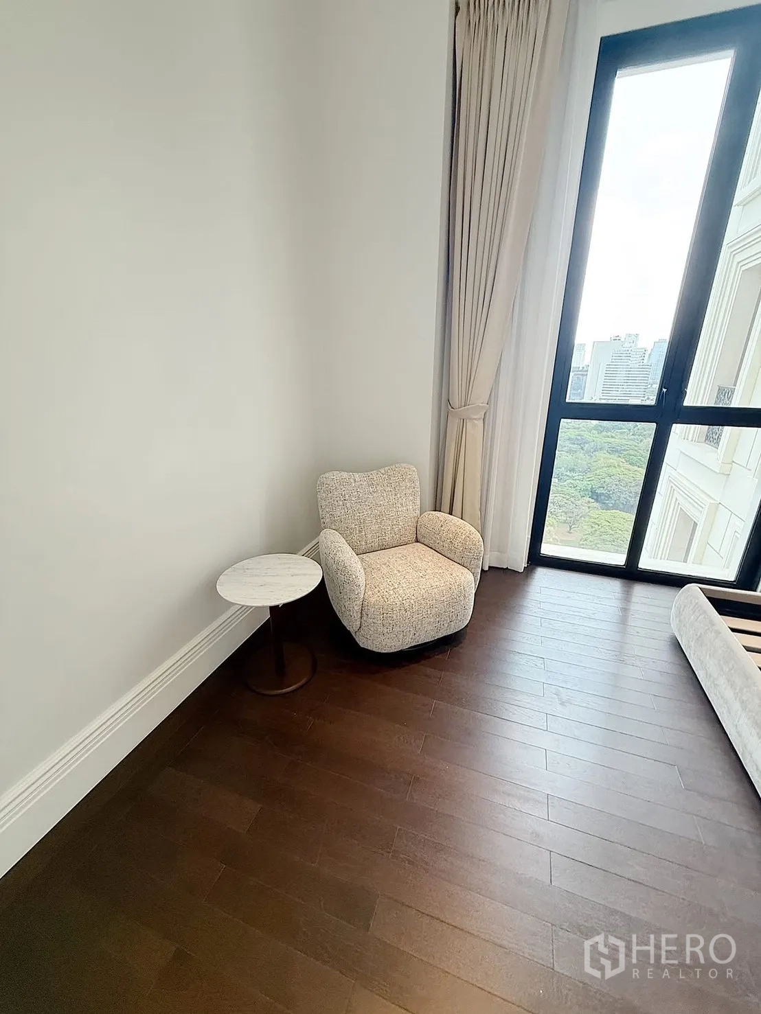Condominium for rent or sale in Pathum Wan, Bangkok - Cozy reading corner with an armchair and side table beside a floor-height window and curtains.