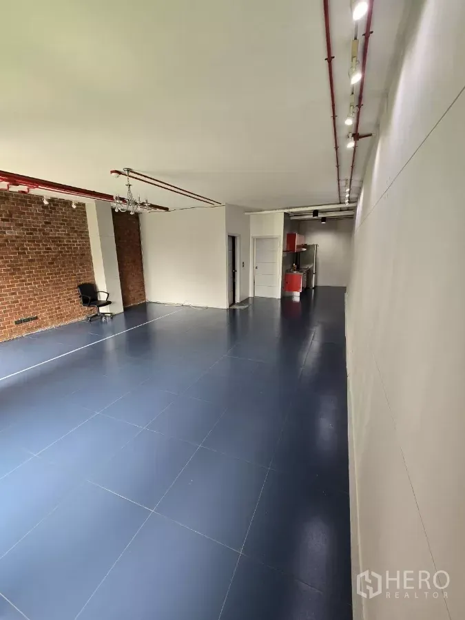 Office Space for rent in Watthana, Bangkok - Open-plan 78 sqm office with blue tile floors, exposed red ceiling pipes, brick accent wall, and kitchenette area.