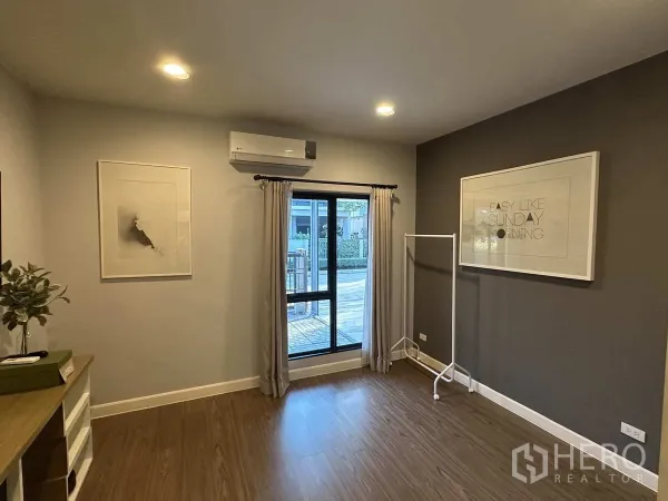 Detached House for rent or sale in Lam Luk Ka, Pathum Thani - Bright ground‑floor room with window, air conditioner and wood flooring.