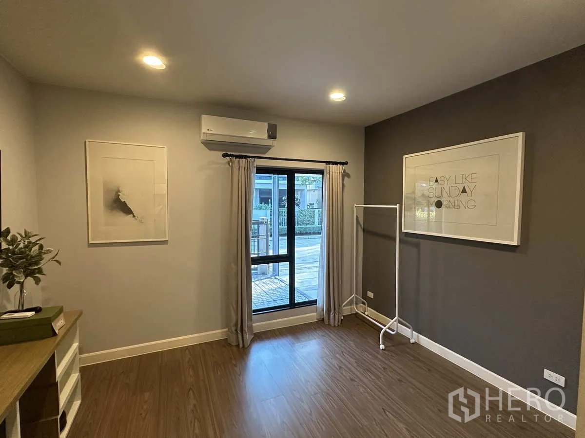 Detached House for rent or sale in Lam Luk Ka, Pathum Thani - Bright ground‑floor room with window, air conditioner and wood flooring.