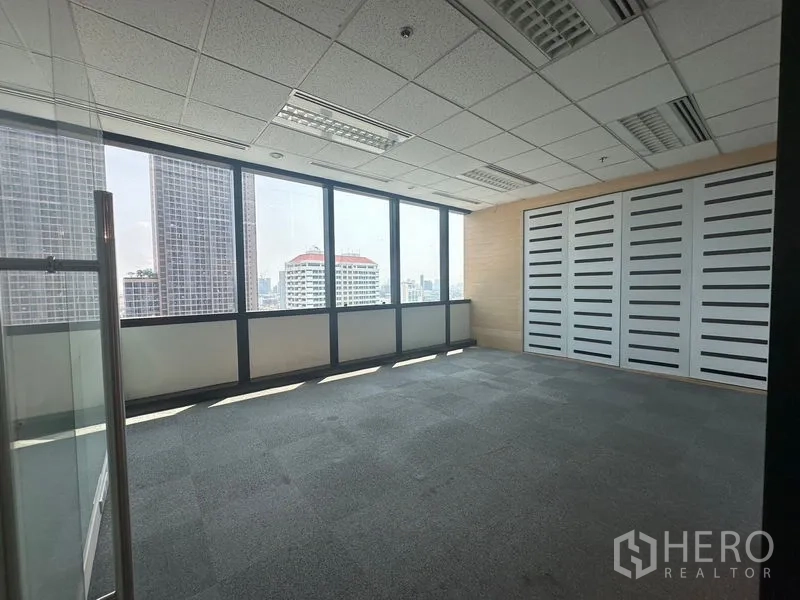 Office Space for rent in Khlong Toei, Bangkok - Private office with carpet flooring, drop ceiling lights, and full-height windows framing city views.