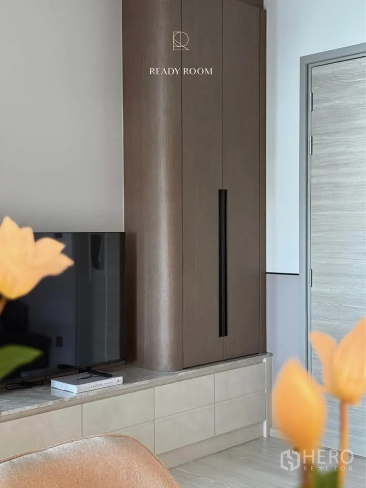 Condominium for rent in Khlong Toei, Bangkok - Living area with low TV console and tall wood storage cabinet.