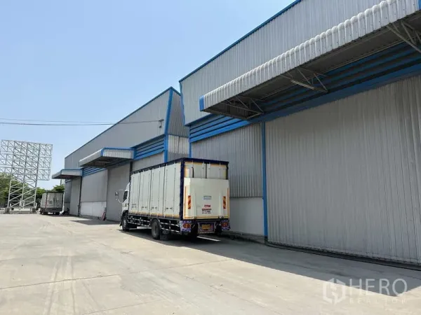Warehouse for rent in Bang Phli, Samut Prakan - Modern steel-clad warehouse blocks with covered loading bays and trucks in a wide concrete yard.
