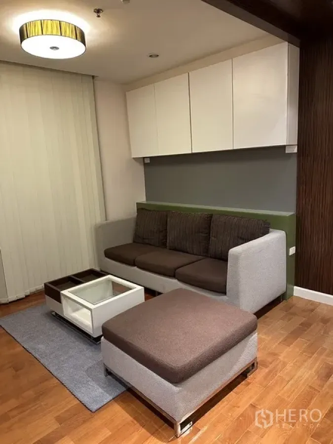 Condominium for rent in Watthana, Bangkok - Contemporary living room with fabric sofa, ottoman, wall cabinets and wood flooring under a ceiling light.